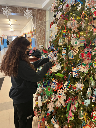 Student adds an ornament to the school lobby Christmas tree