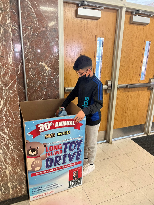 Student places a toy in the Long Island Toy Drive collection box.